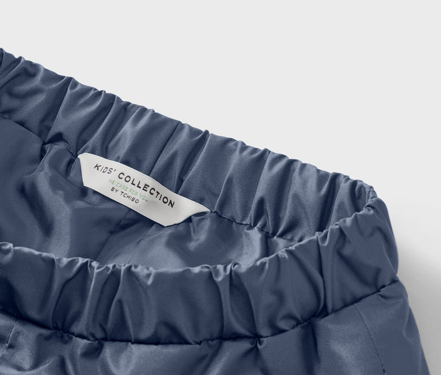 Kék gyerek nadrág részlete, gumis derékpánttal és egy címkével, melyen a Kids' Collection felirat olvasható.