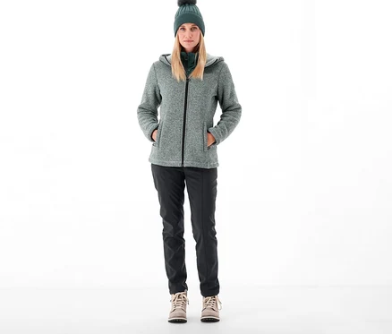 Nő áll, CMP női softshell nadrágot, kabátot és sapkát visel.