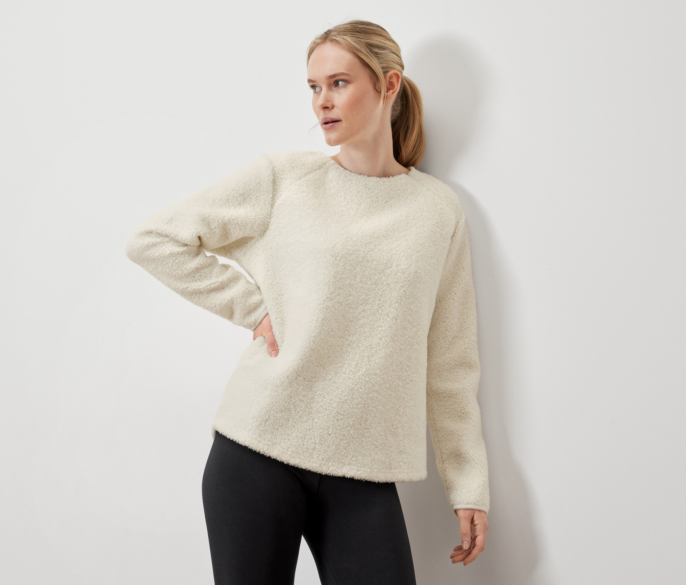 Nő pózol krémszínű pulóverben és fekete leggingsben.