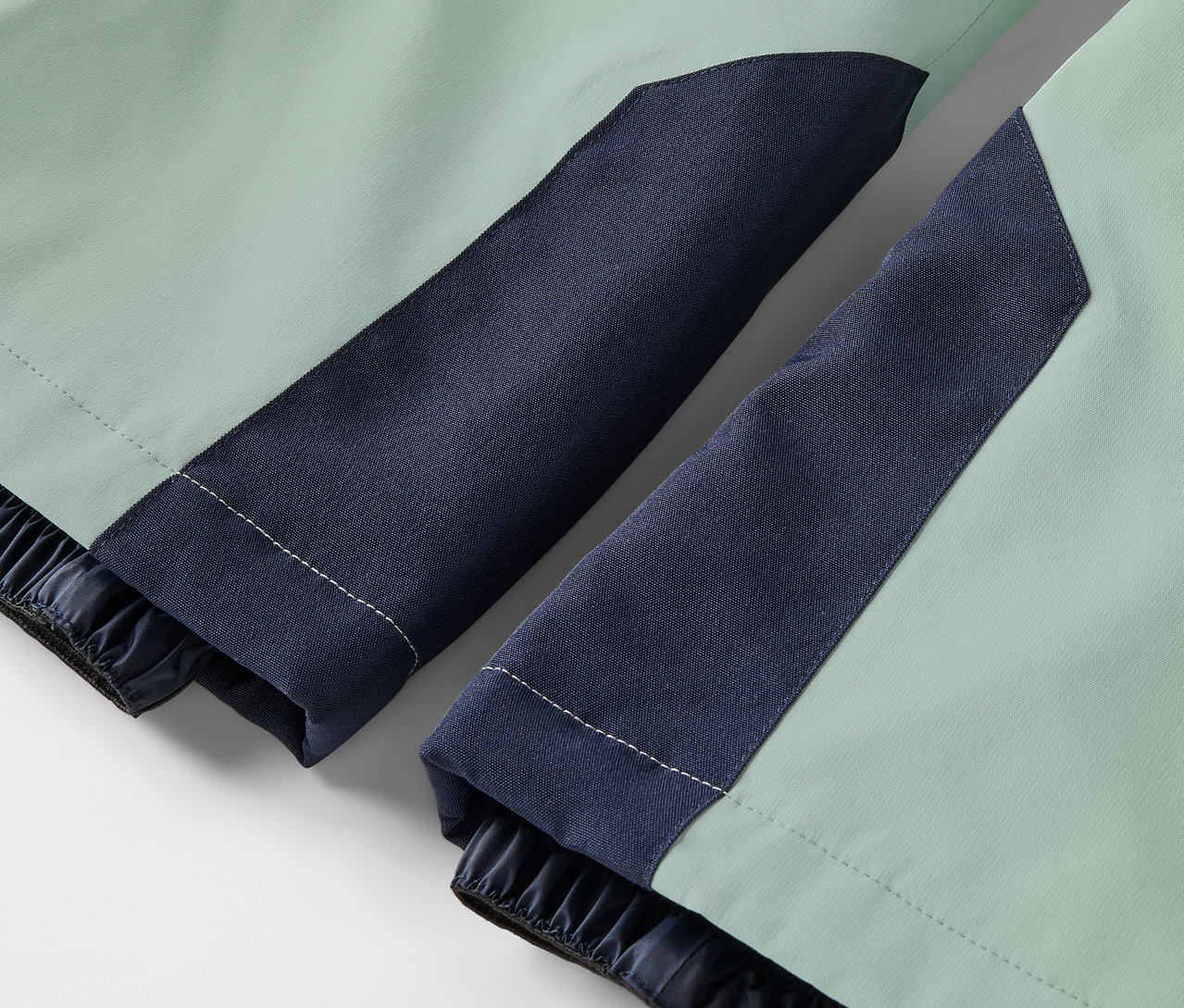 Világoszöld kabát részlete sötétkék ujjakkal és rugalmas mandzsettákkal.