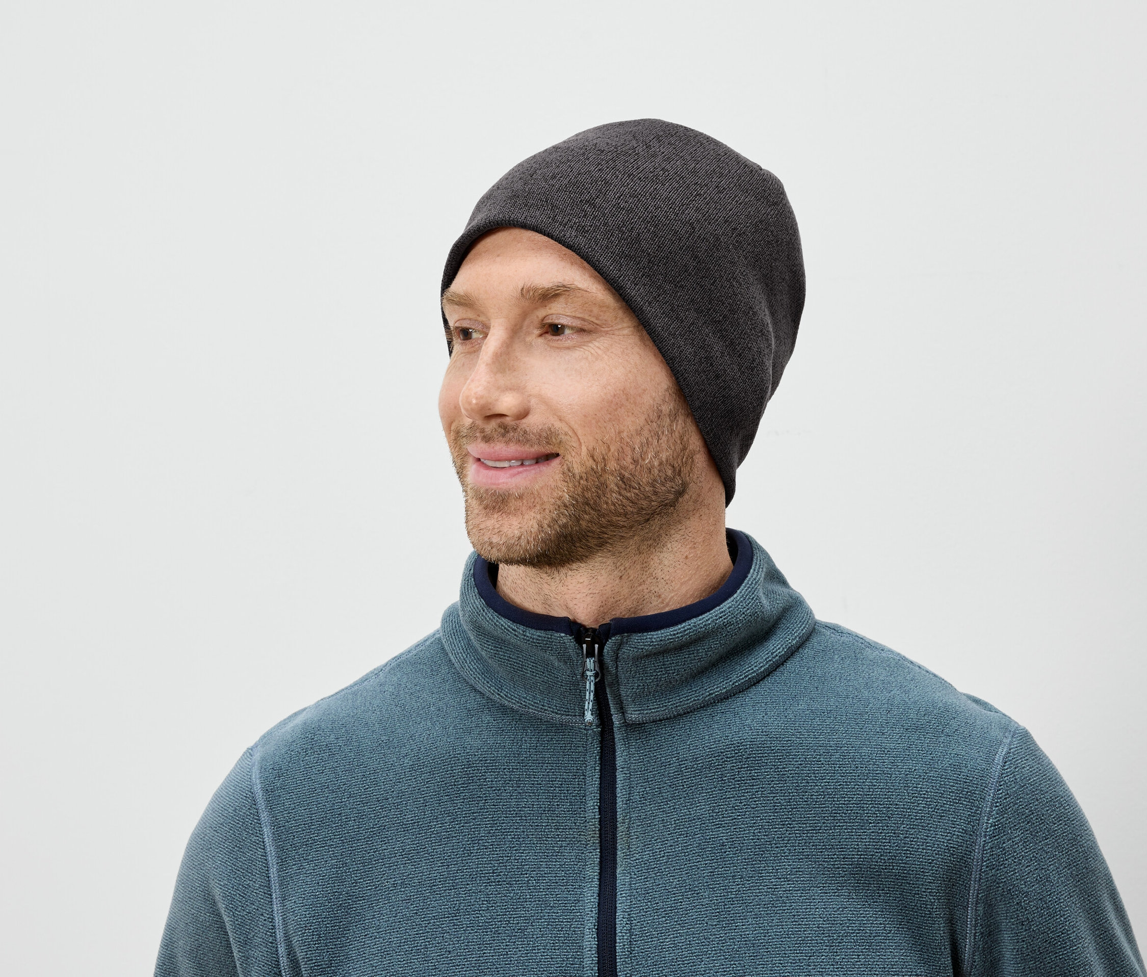 Szakállas férfi szürke sapkában és kék polár pulóverben jobbra néz.