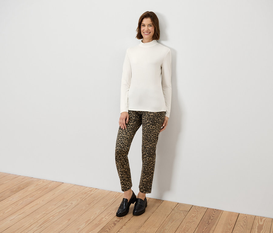 Nő pózol, krémszínű, hosszú ujjú felsőben és állatmintás nadrágban.
