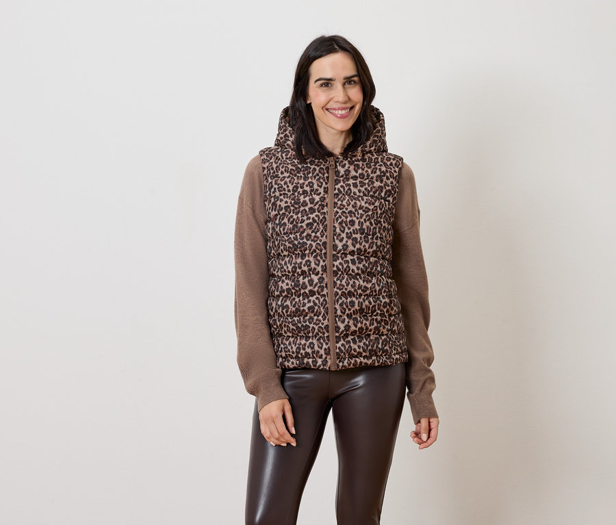 Nő pózol barna, kapucnis, állatmintás mellényben és barna bőr nadrágban.