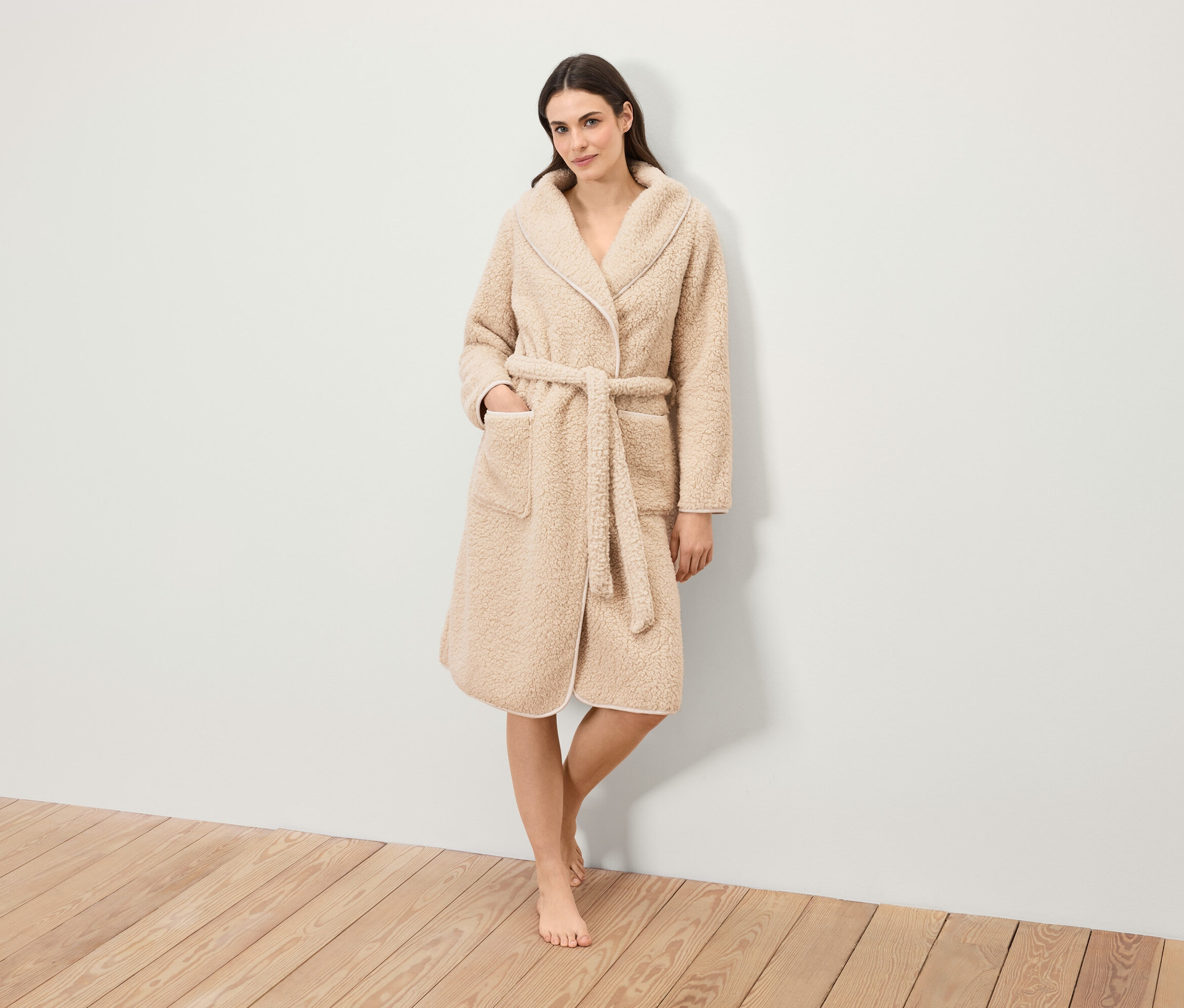 Egy nő áll, és egy övvel ellátott, bolyhos köntöst visel.