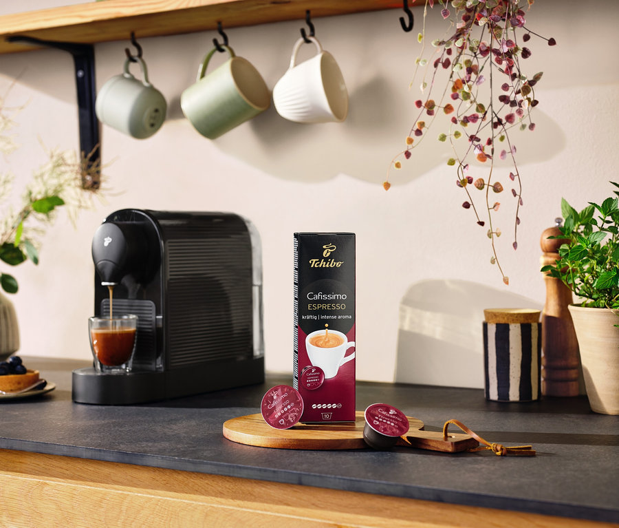 Fekete Cafissimo pure+ kávéfőző kávét készít egy pohárba. Az asztalon egy csomag kapszula és két kapszula található.