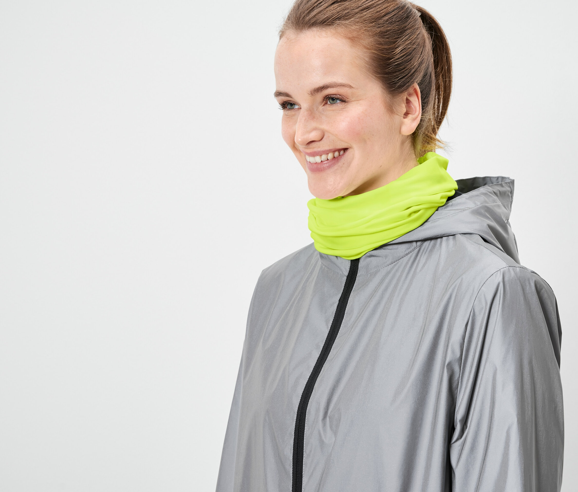 Nő szürke kabátot és neon zöld sálat visel.