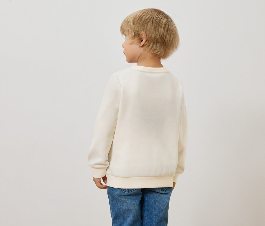 Hátulnézet egy szőke gyerekről, aki Kinder-Sweatshirt-öt visel, bolyhos belsővel, Sonne és kék farmernadrágot.