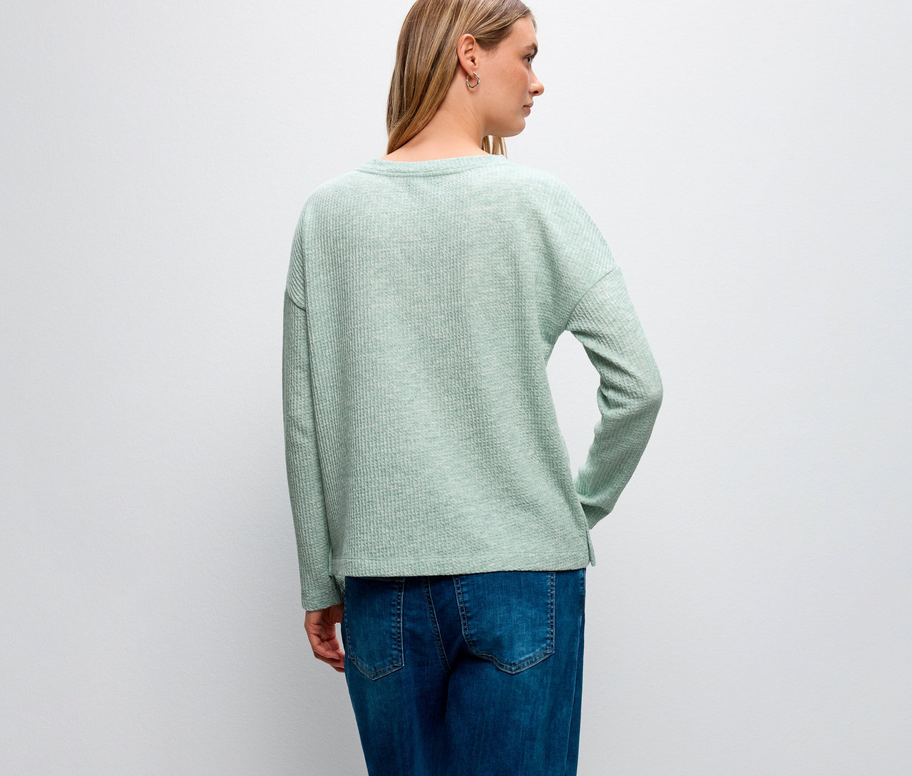 Hátulnézet egy szőke hajú nőről, aki Street One bordás mintás pólót és kék farmert visel.