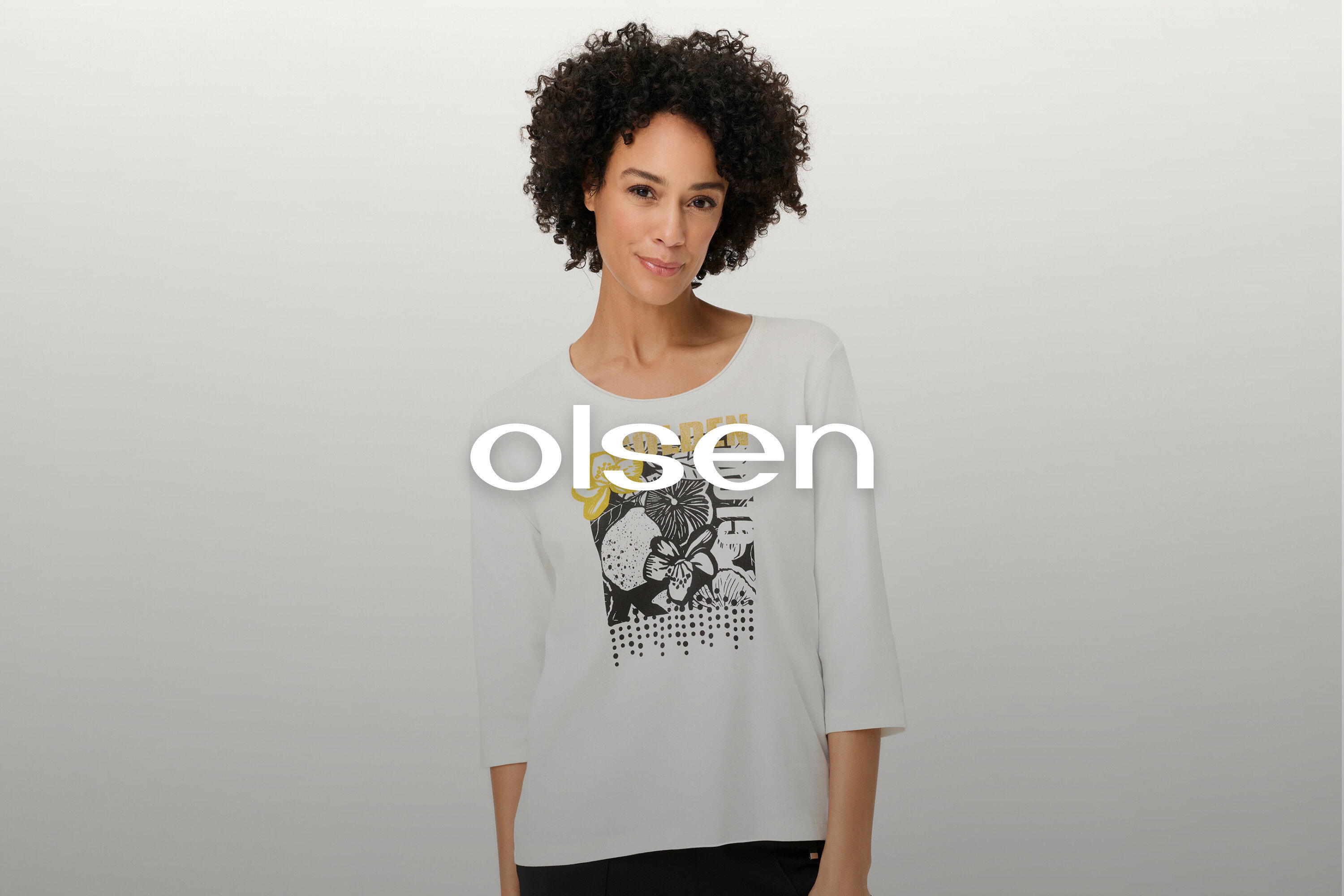 A göndör hajú nő virágmintás, fehér, hosszú ujjú pólót visel.