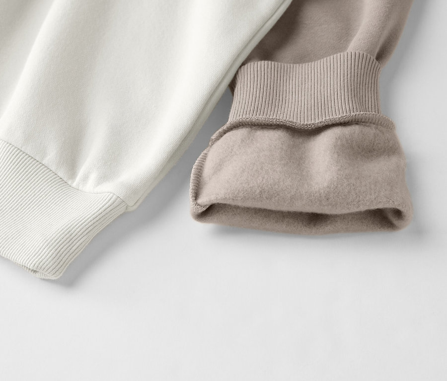 Közelkép egy kétszínű, fehér és bézs színű, bordázott mandzsettás pulóverről.