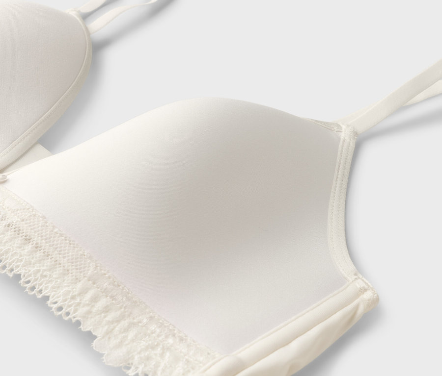 Egy csipkés, vékony pántos fehér melltartó részletes képe.