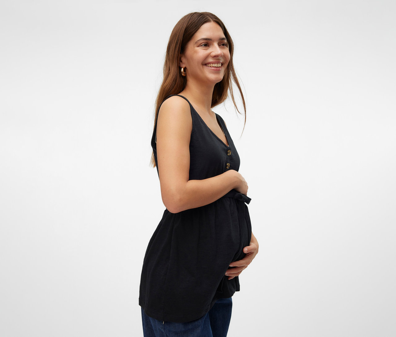 Mosolygó nő tartja a hasát, fekete MAMALICIOUS »MLEVI LIA« szoptatós felsőt és farmert visel.