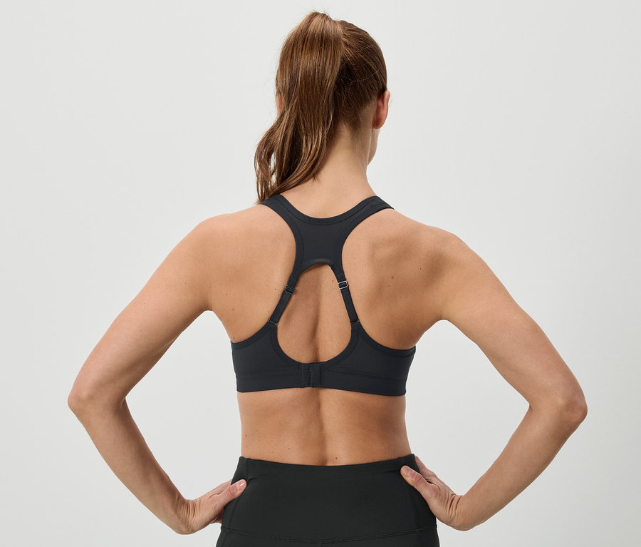 Hátulnézet egy barna hajú, lófarokba kötött nőről, aki fekete sportmelltartót és leggingst visel, és a csípőjén tartja a kezét.