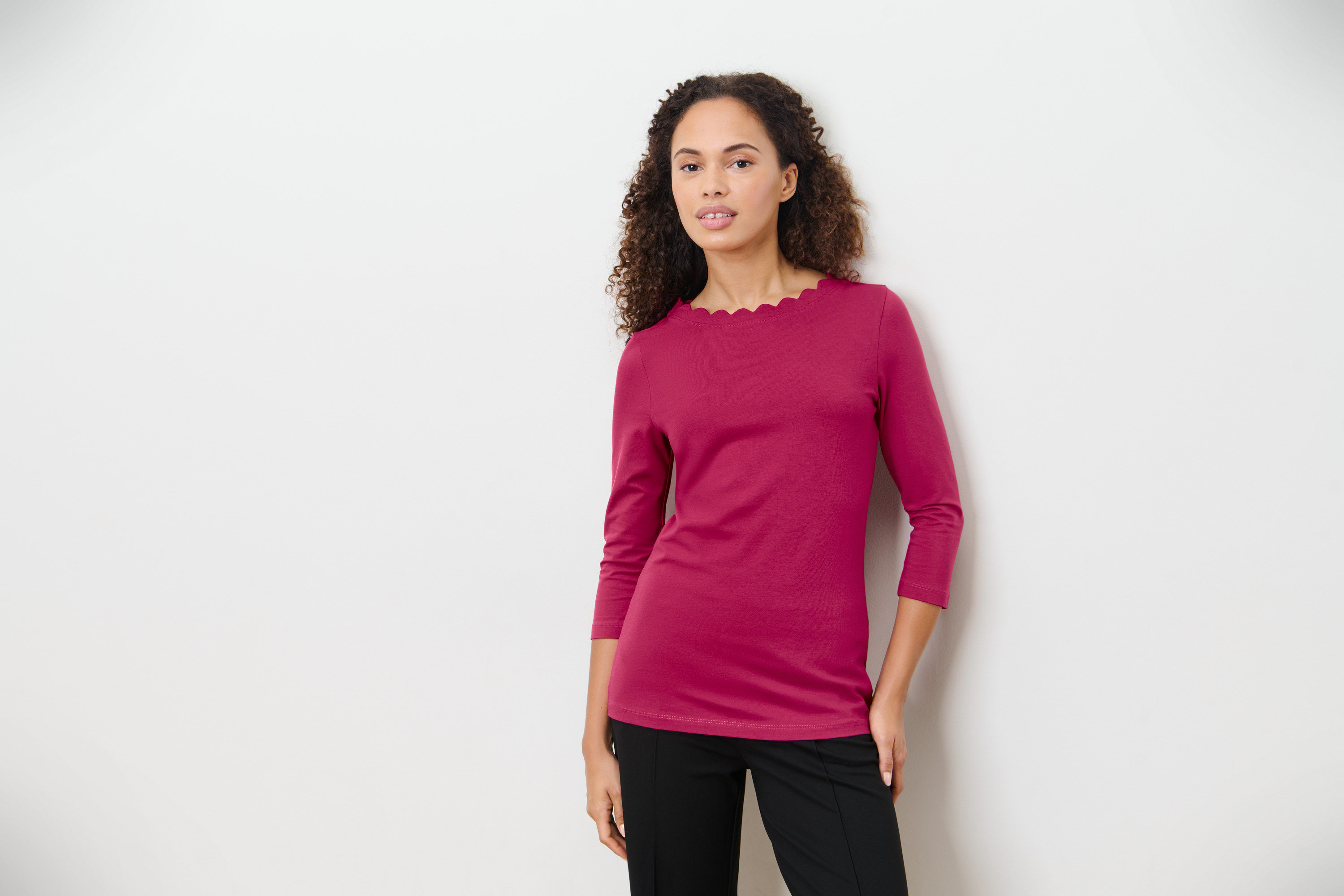 Nő málnapiros, 3/4-es ujjú felsőben pózol.