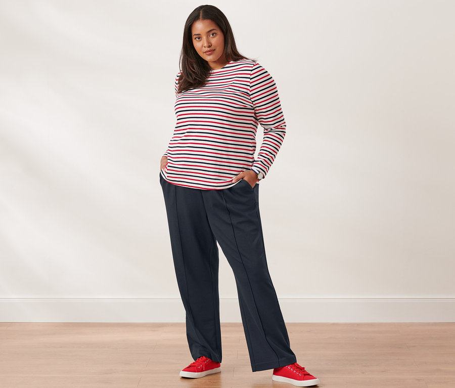 Nő pózol csíkos hosszú ujjú felsőben, szabadidőnadrágban, vászon sneaker cipőben és nemesacél karórában.