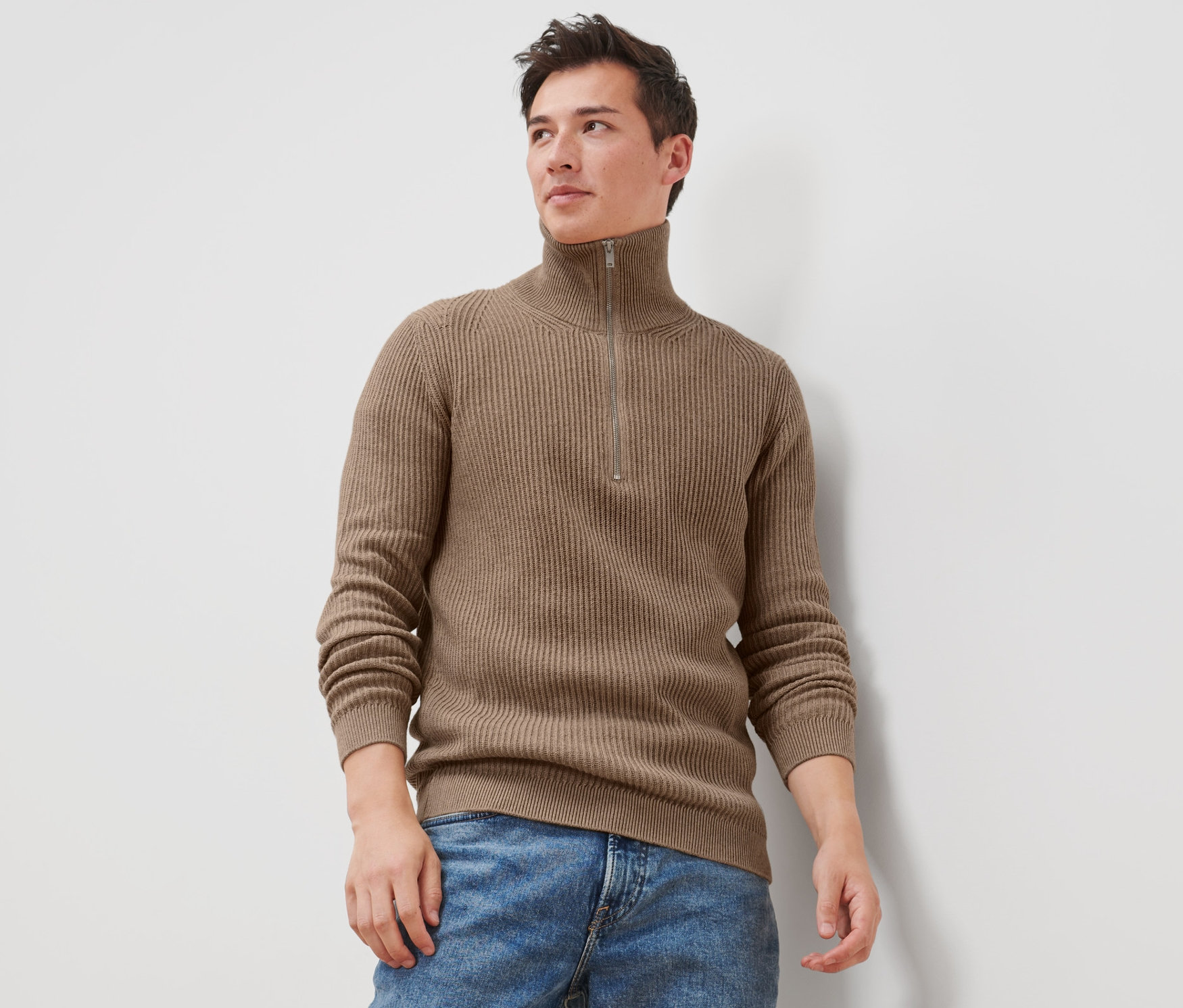 Férfi barna kötött pulóvert és farmernadrágot visel.