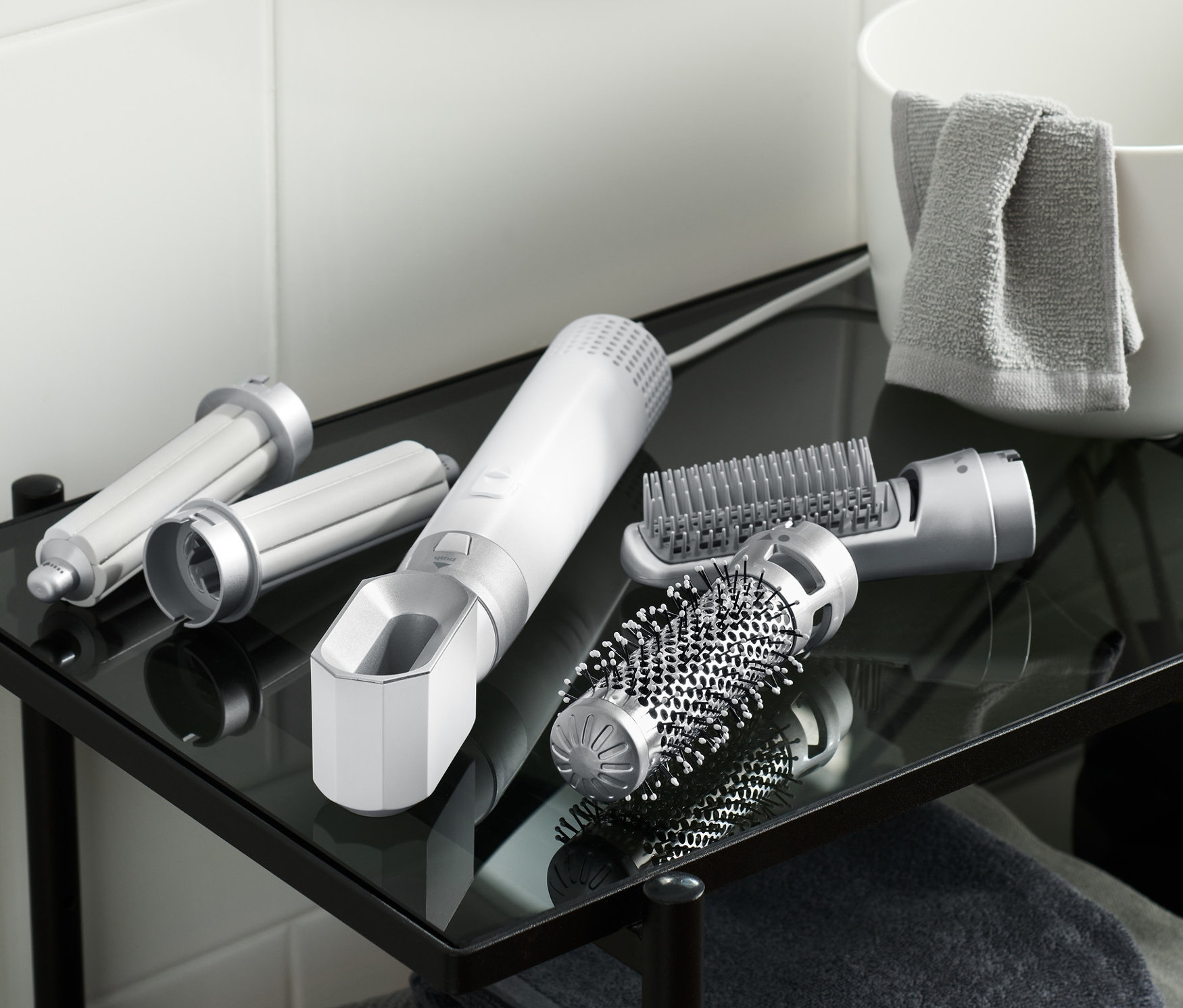 Egy üveg fürdőszobai polcon egy 5 az 1-ben multifunkciós hajformázó szett és a hozzá tartozó tartozékok találhatók.