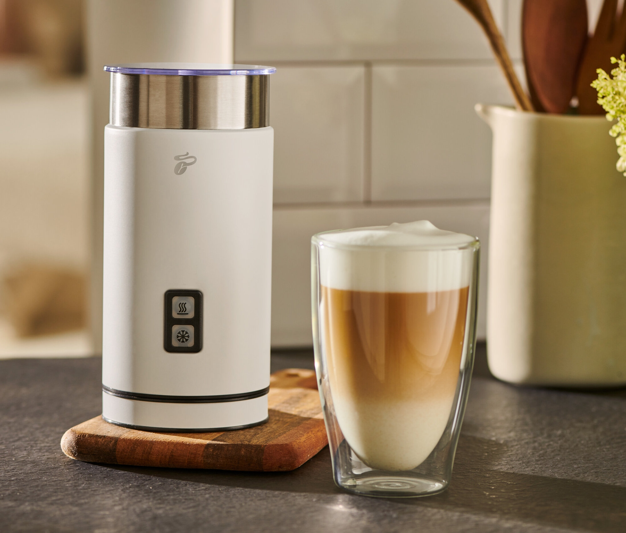 Egy fehér elektromos tejhabosító egy pohár tejeskávé mellett áll.