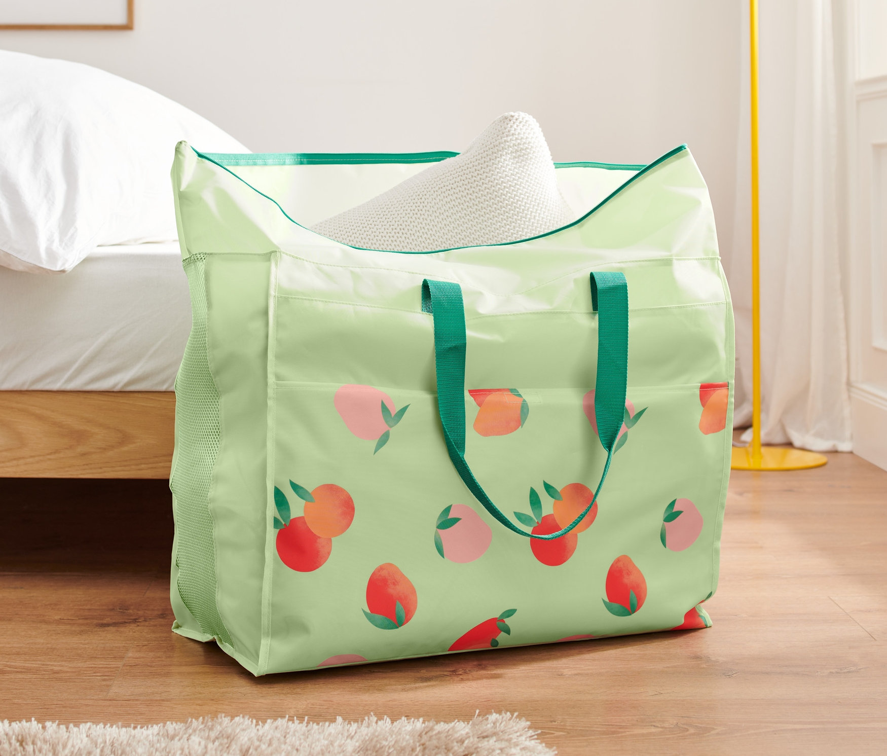 Egy barackmintás nagyméretű ágyneműtároló táska áll a padlón egy ágy mellett.