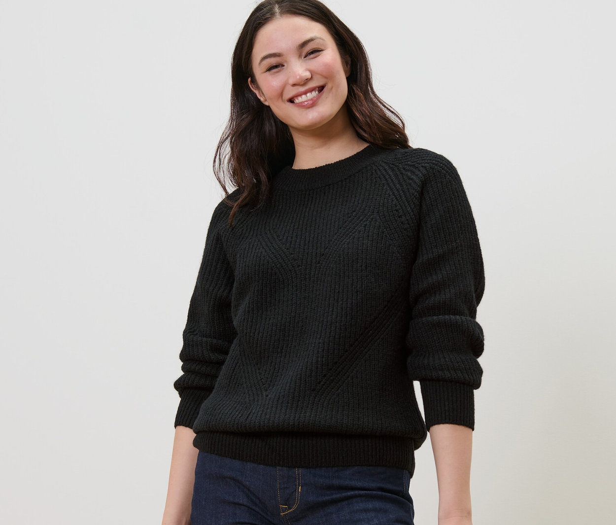 Mosolygó nő fekete kötött pulóvert visel.