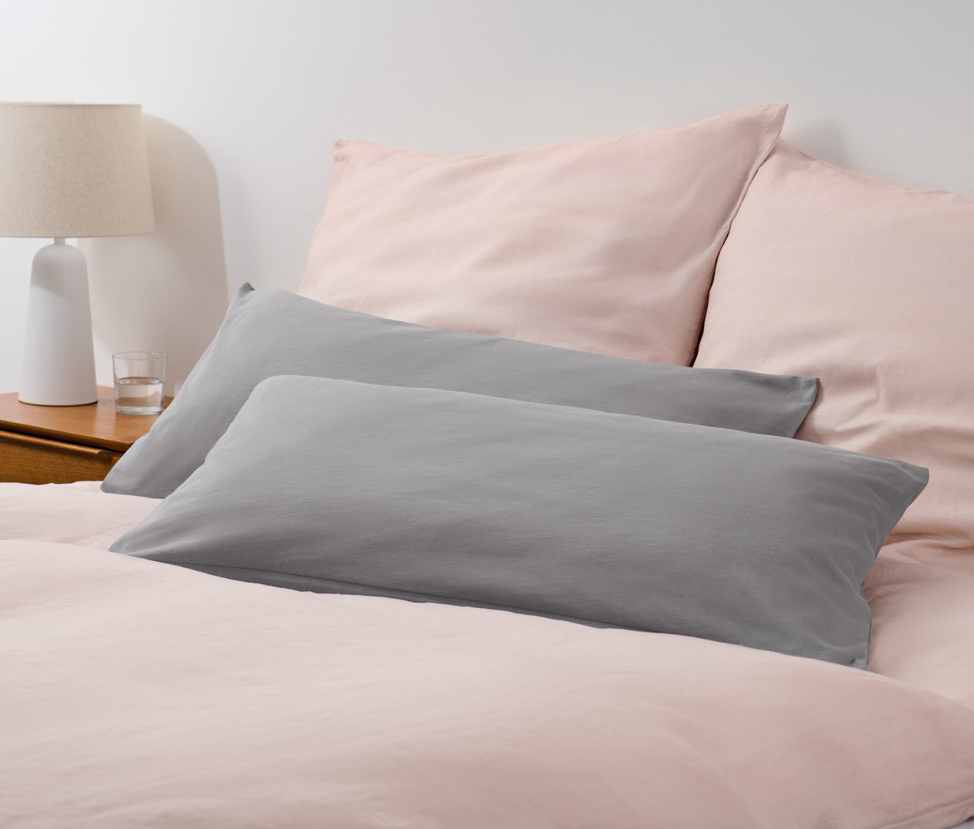 Két szürke jersey párnahuzat egy rózsaszín ágyneművel ellátott ágyon.