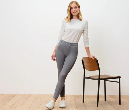 Nő pózol szürke farmer hatású leggingsben egy szék mellett.