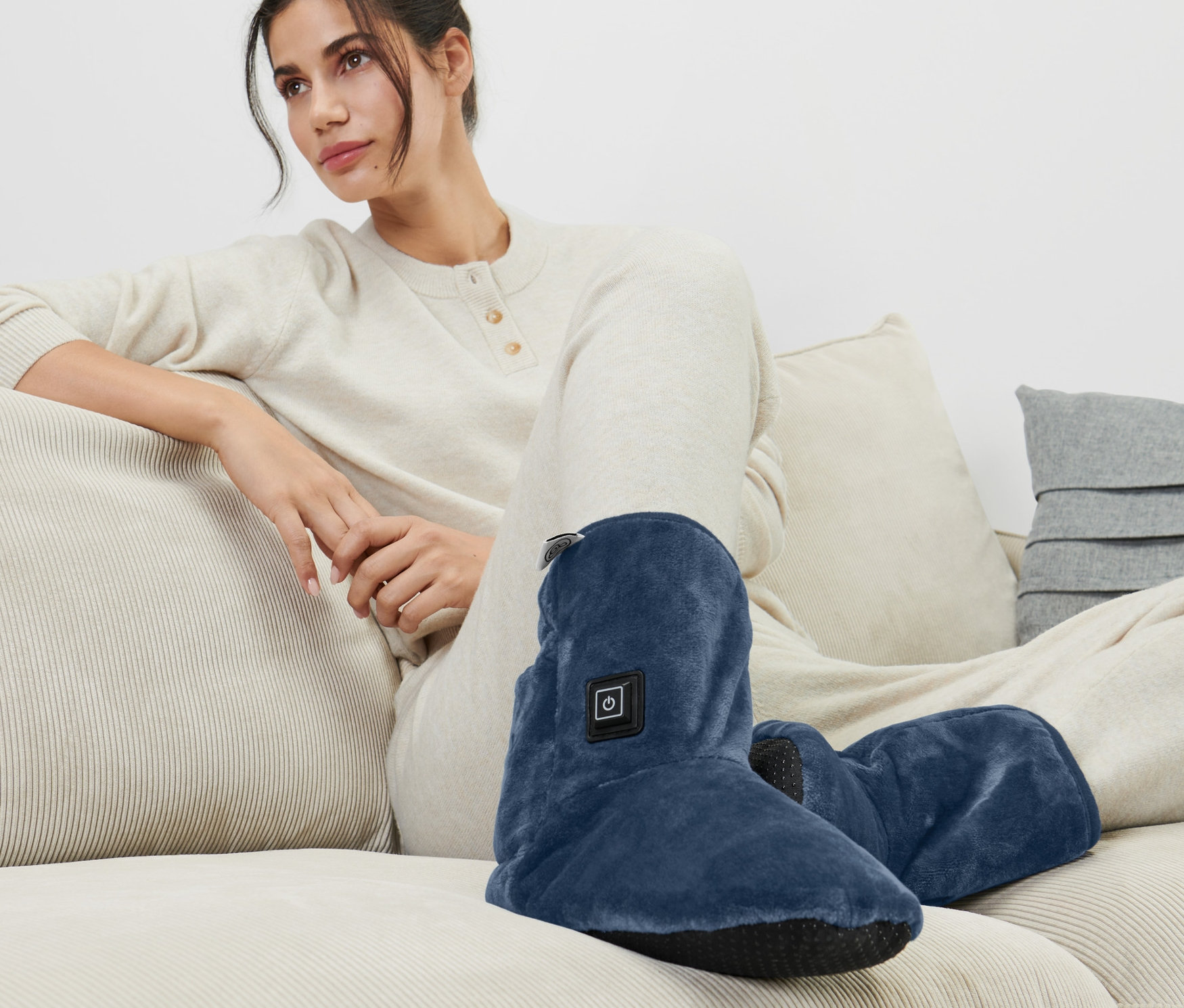 Nő ül a kanapén és elektromos lábmelegítő plüsscipőt visel.