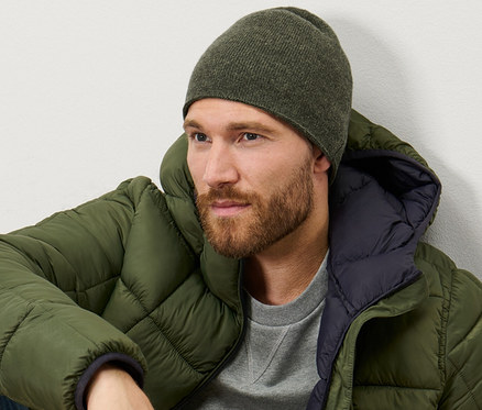 Egy férfi ül, és melírozott khaki kötött sapkát visel.