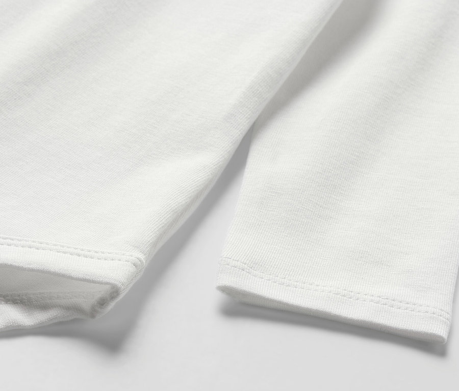 Egy hosszú ujjú, fehér baba body részletének fényképe.