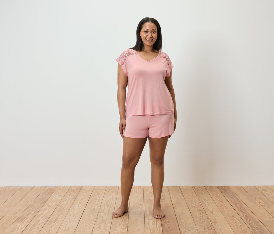 Egy nő áll rózsaszín pizsamában, csipkével a vállán.
