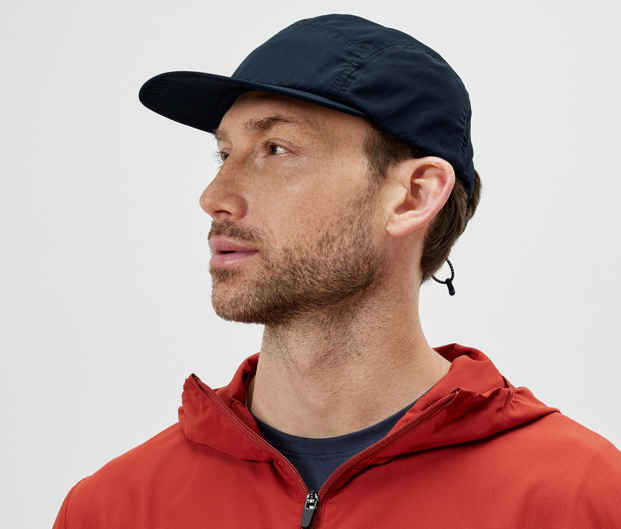 Férfi narancssárga kabátban, sötétkék túrasapkát visel, összehajtható.