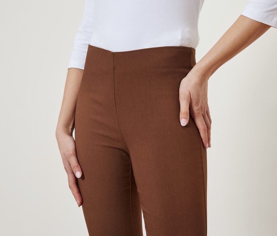 Nő pózol barna nadrágban és fehér felsőben.