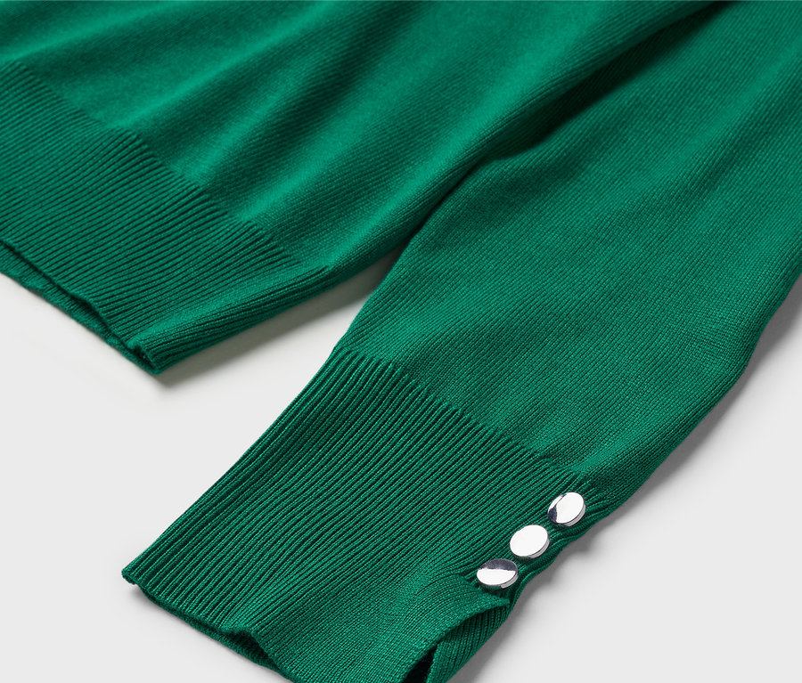 Egy zöld, hosszú ujjú pulóver részlete, díszgombokkal a mandzsettán.