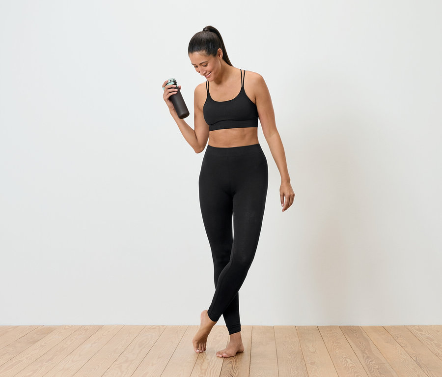 Fekete sportruházatot viselő nő tart egy kulacsot.