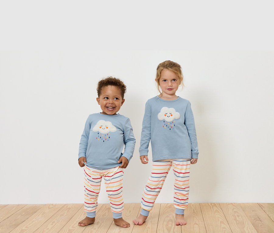 Két gyermek áll a fapadlón, kék, hosszú ujjú felsőket és csíkos nadrágokat viselnek.