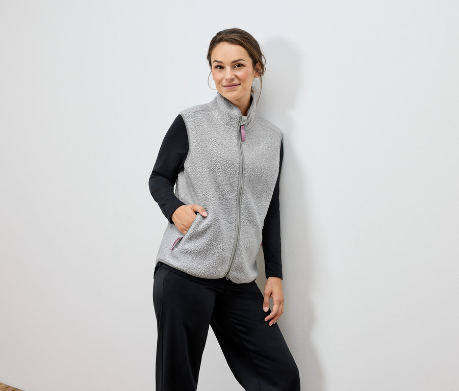 Nő visel szürke polár mellényt és fekete nadrágot.