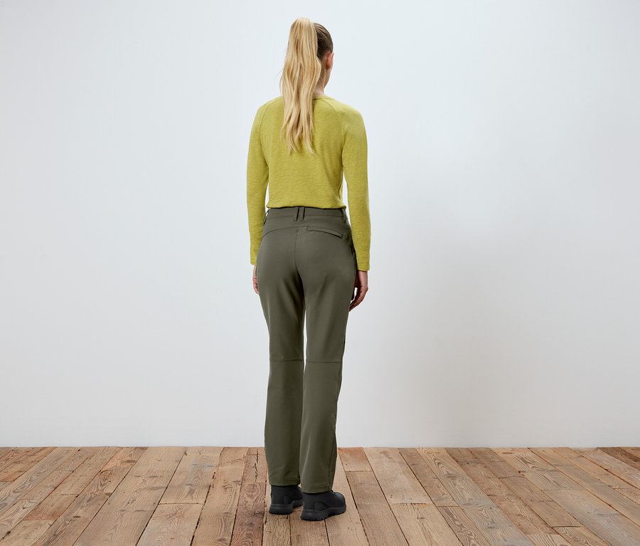 Egy nő áll háttal a kamerának, zöld nadrágot és sárga felsőt visel.