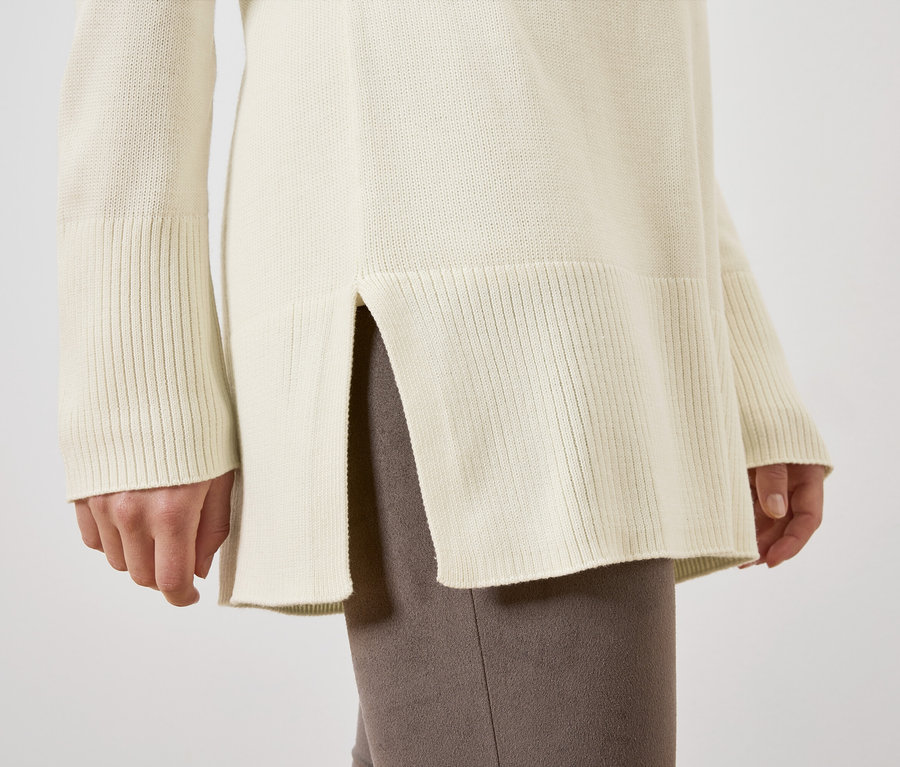 Egy nő részlete a hosszú, krémszínű kötött pulóverben.