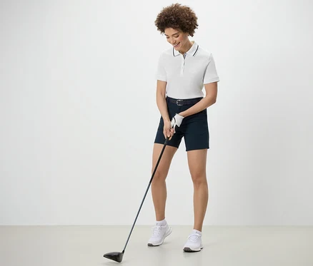Nő golfozik, fehér funkcionális pólóinget visel.