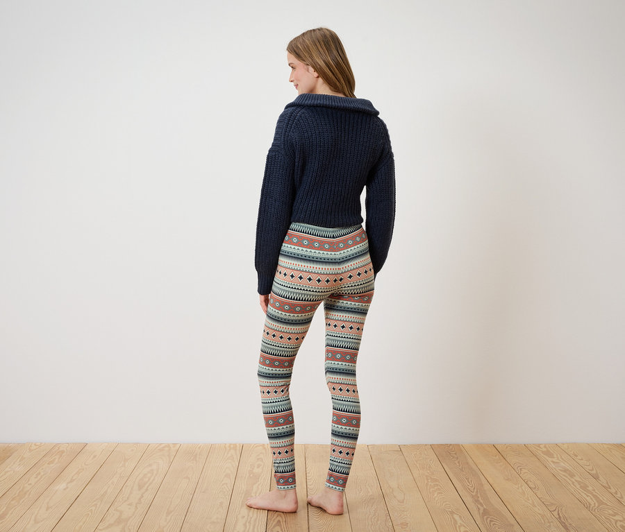 Egy nő sötétkék pulóverben és mintás leggingsben áll háttal a kamerának.