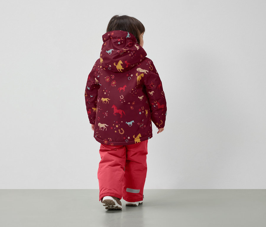 Fiú ló mintás téli kabátban és piros nadrágban, háttal a kamerának.