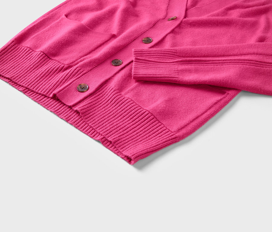 Egy rózsaszín, gombos, zsebes kardigán részlete.