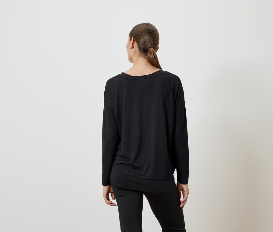 Hátulnézet egy fekete, hosszú ujjú felsőt és fekete nadrágot viselő nőről.