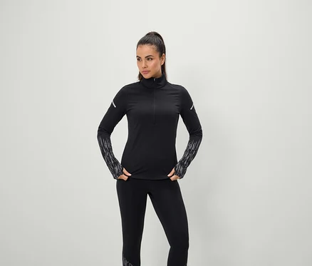 Nő pózol fekete, hosszú ujjú sportruházatban és leggingsben.
