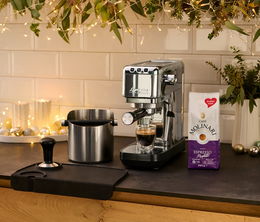 A konyhapulton egy ezüstszínű »Lapressa« karos eszpresszó kávéfőző áll egy csésze eszpresszó mellett.