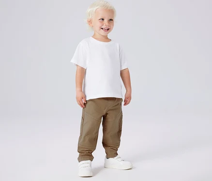 Mosolygó fiú fehér pólóban, khaki NAME IT twillnadrágban és fehér cipőben.