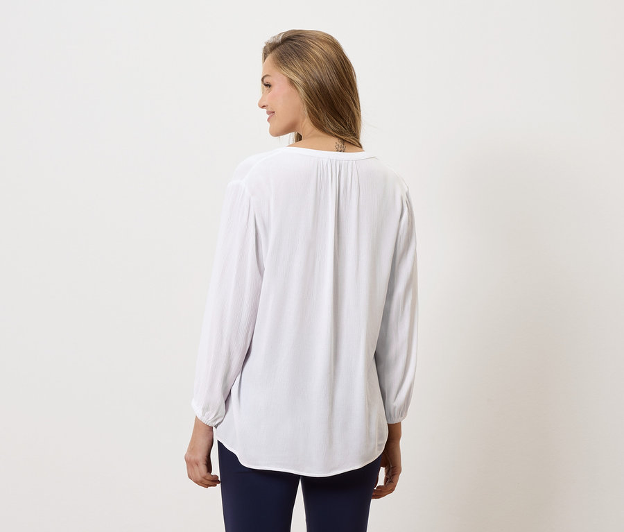 Hátulról látható nő, hosszú, fehér blúzt és kék nadrágot visel.