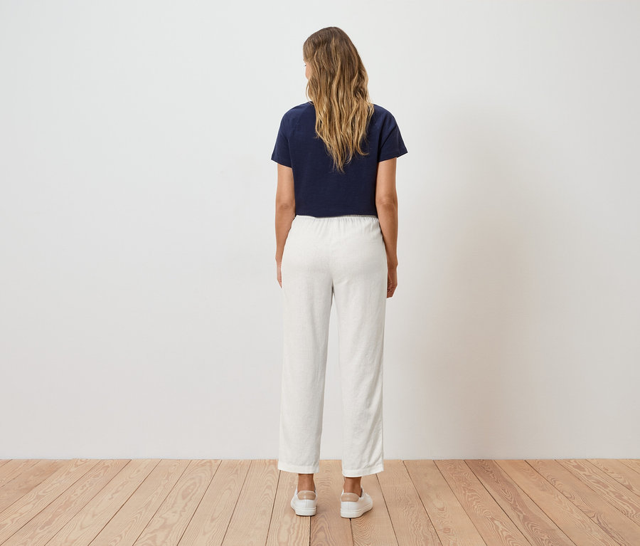 Egy szőke, hullámos hajú nő áll háttal a nézőnek, sötétkék pólót és fehér nadrágot visel.