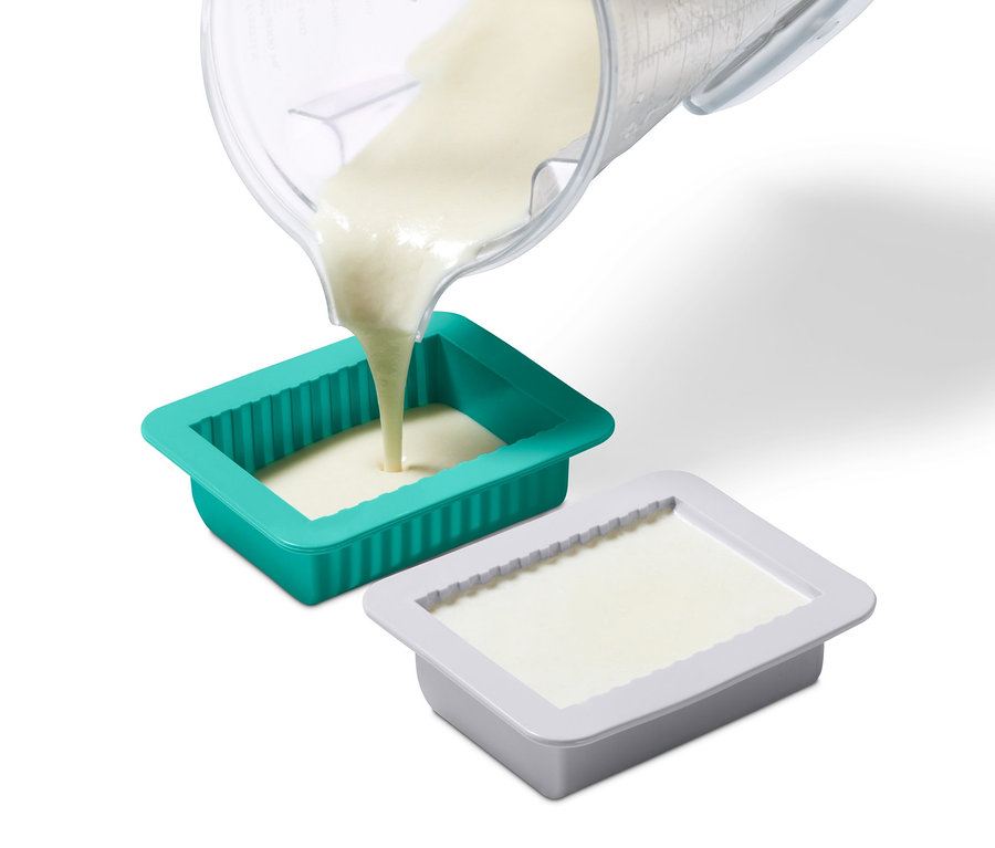 Folyadékot öntenek egy mérőpohárból a növényi vaj készítő készlet zöld formájába. Egy szürke forma megtelt.