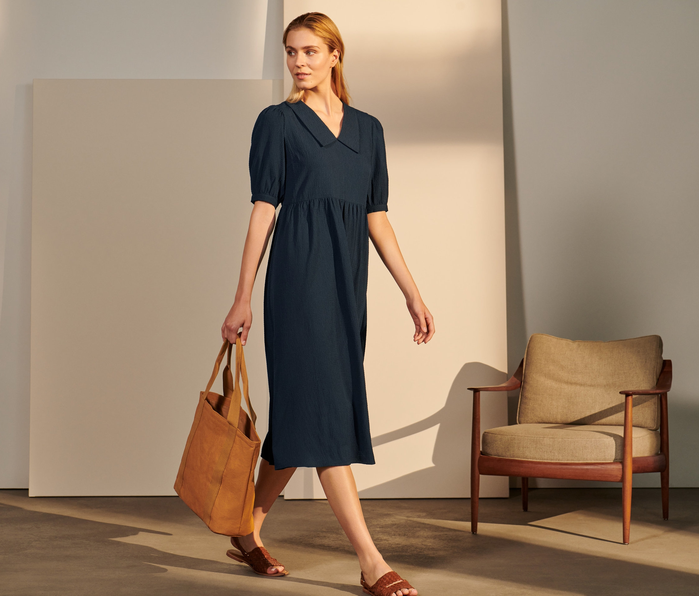 Nő sétál és barna táskát visz, krepp blúzruhát visel.